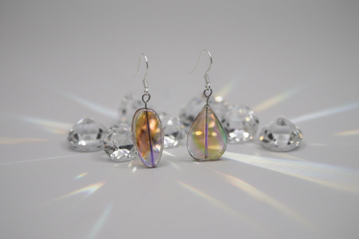 A pair of handmade glass drop earrings with silver fishhook wires, featuring organic, teardrop-shaped glass pendants with iridescent swirls of orange, green, purple, and blue on a light gray background.