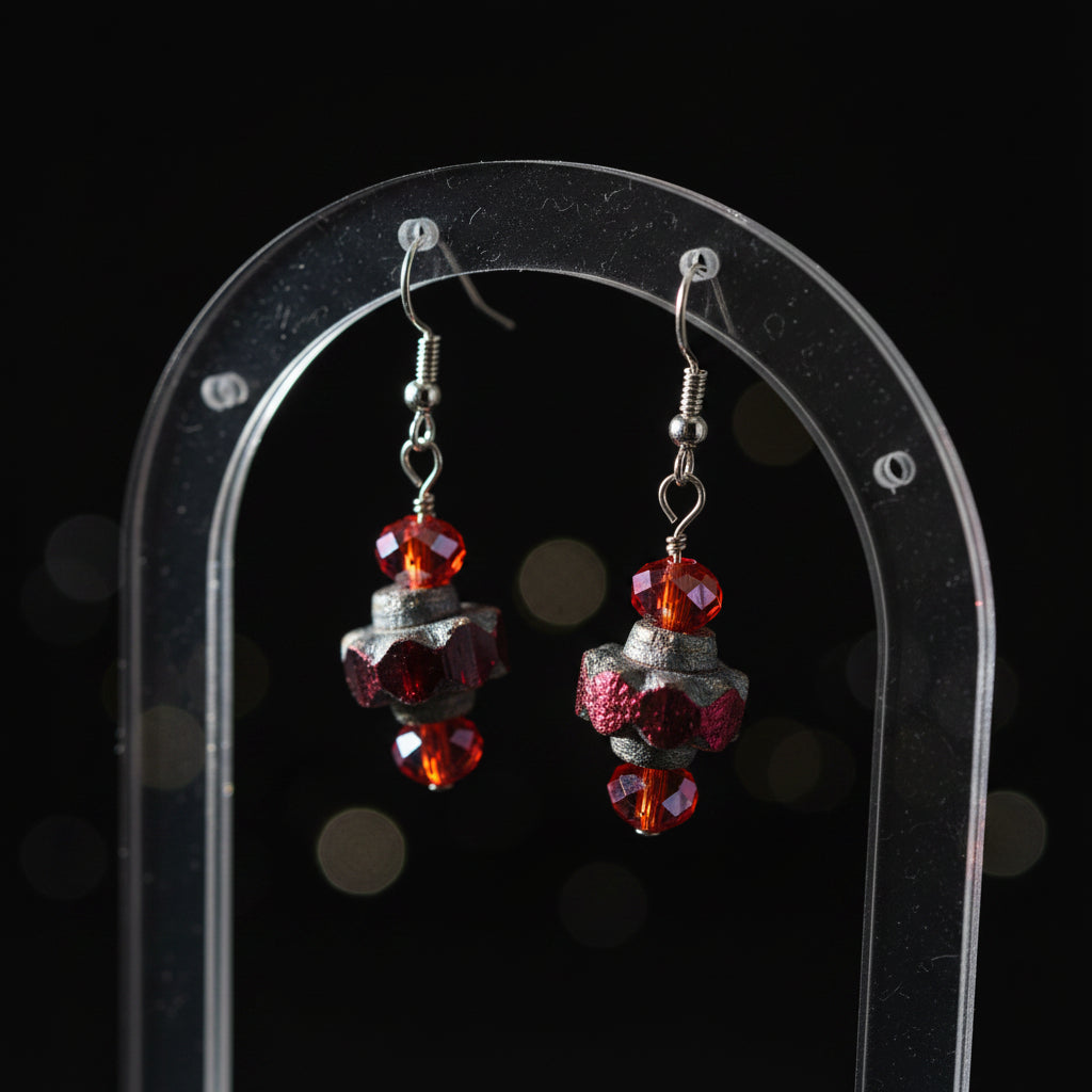 A pair of handmade dangle earrings featuring faceted dark gray beads, small orange-red beads, and silver fishhook backings, displayed against a plain light gray background.