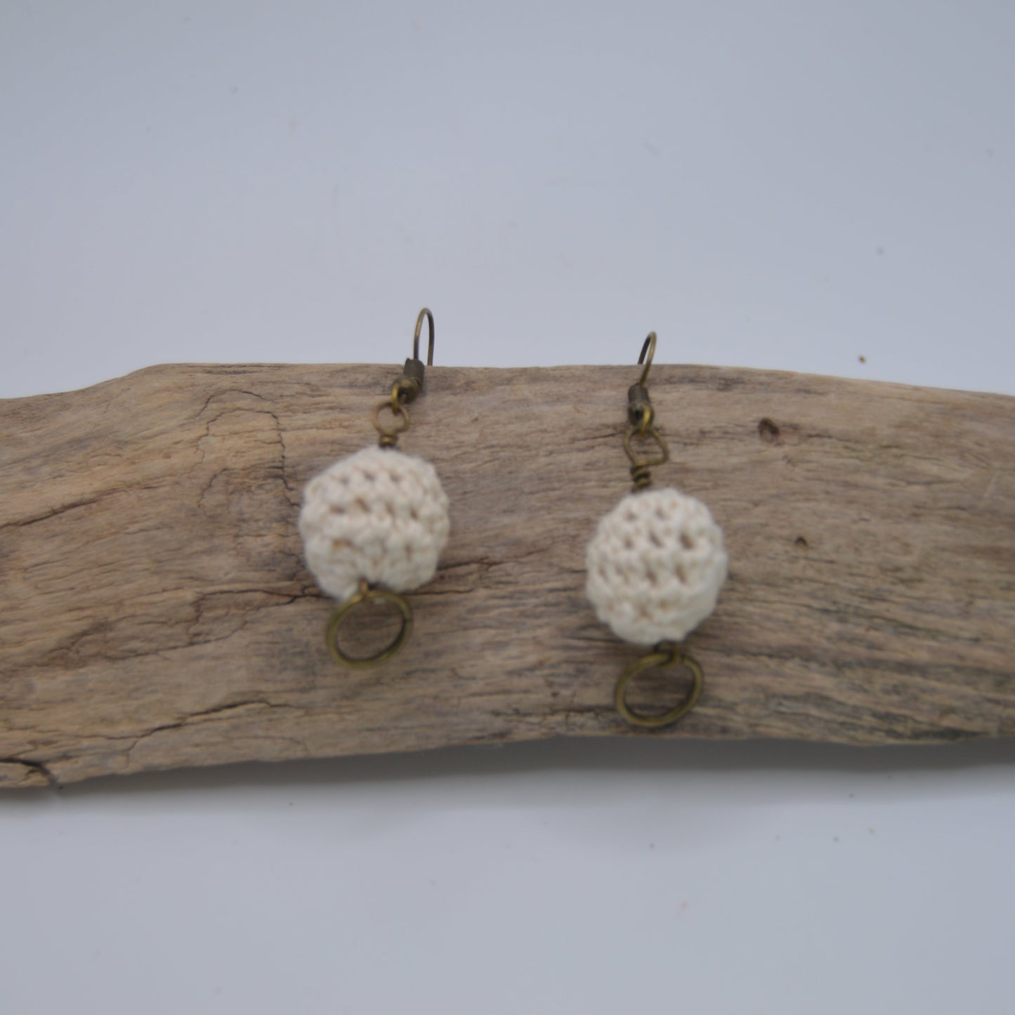 Pair of earrings with white spherical beads on a piece of driftwood against a white background