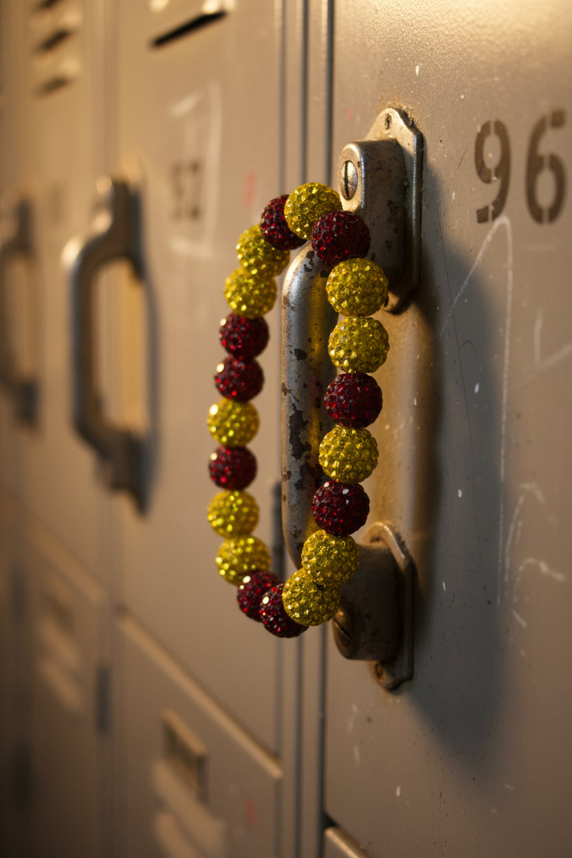 A beaded stretch bracelet featuring alternating round, glittery gold and deep red beads, displayed on a plain light gray background.