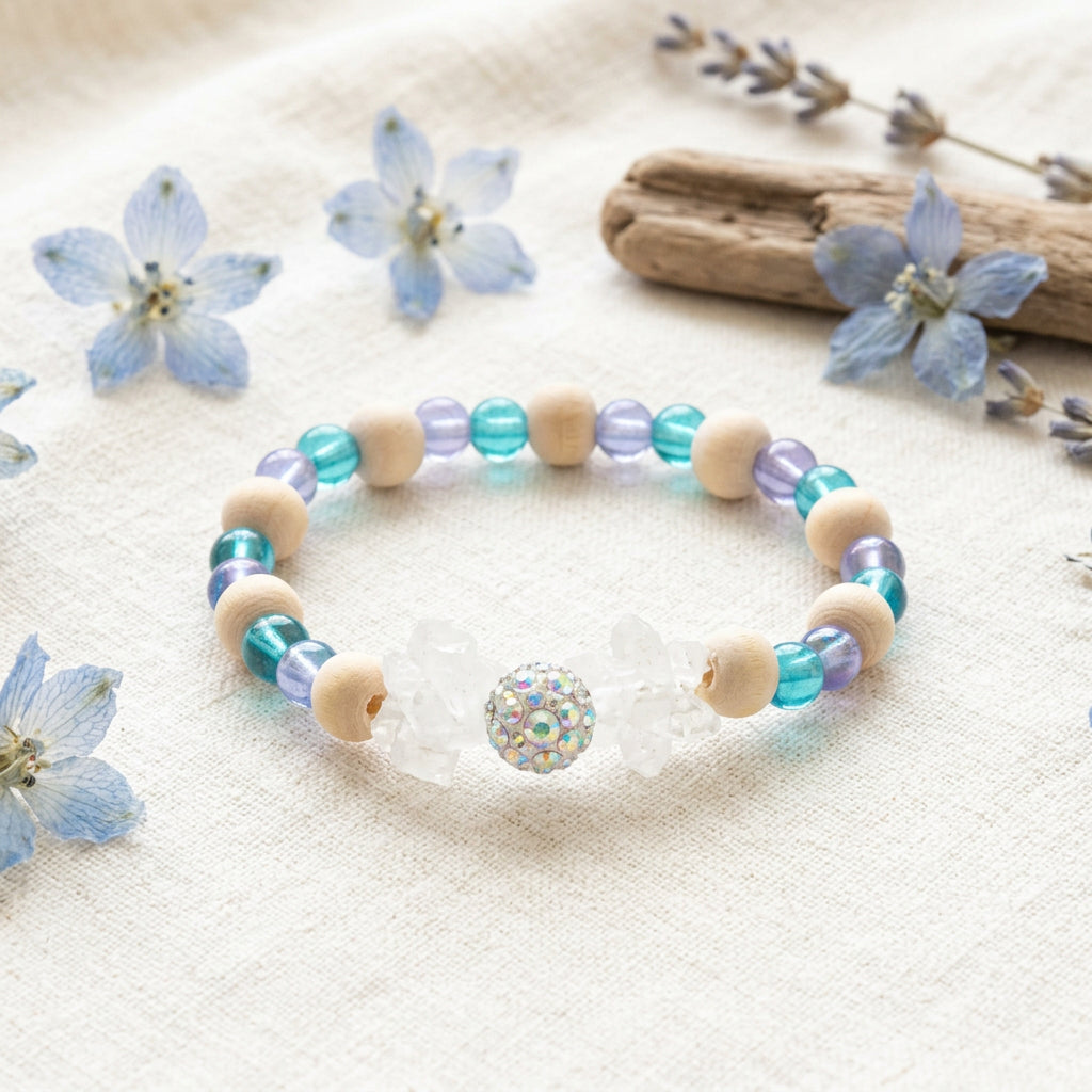A beaded stretch bracelet featuring light wood beads, translucent blue beads, and a central clear acrylic cat charm with a small iridescent rhinestone.