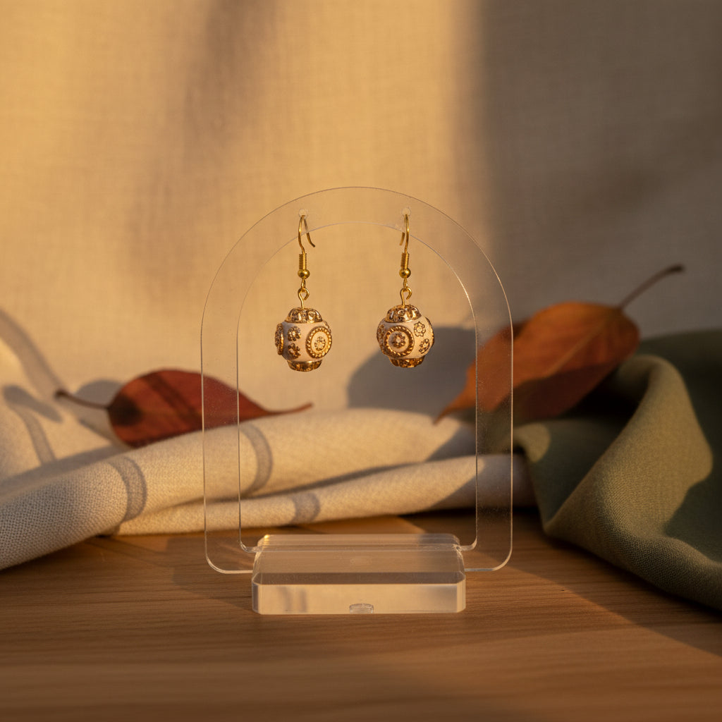 A pair of dangling earrings with gold-toned hooks and spherical filigree charms in a warm metallic rose-gold or copper tone, displayed against a plain light gray background.