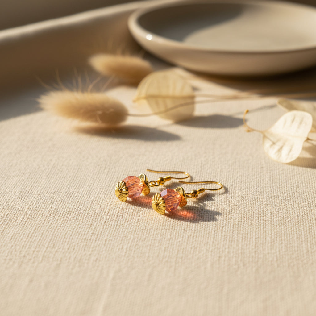 A pair of dangling earrings displayed on a white card labeled 'River Inspired handmade jewelry.' The earrings have gold-tone hooks and beads with pink and orange translucent stones.