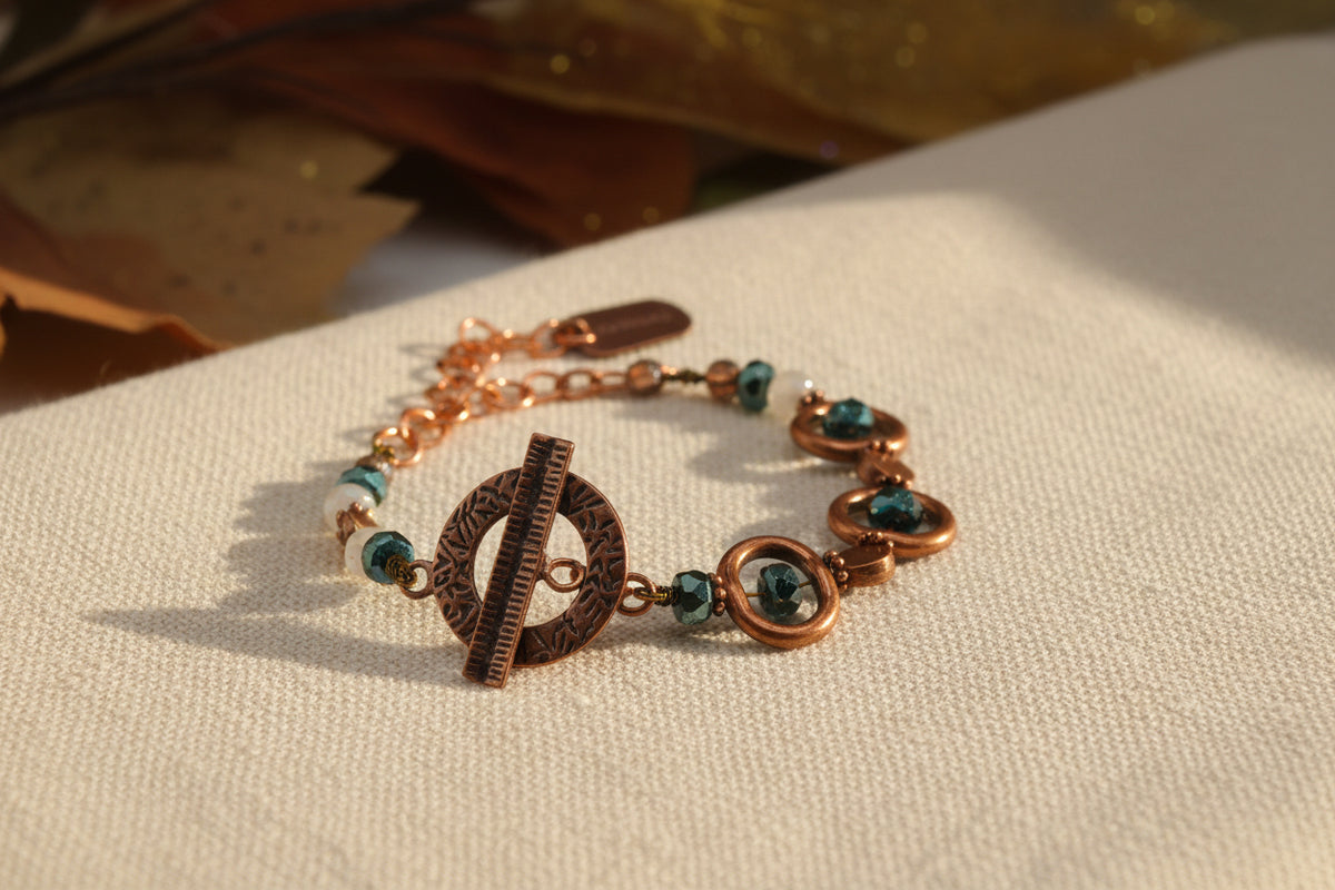 A handmade beaded bracelet with copper-toned metal rings, dark green faceted beads, and a matching copper toggle clasp, displayed on a plain light gray background.