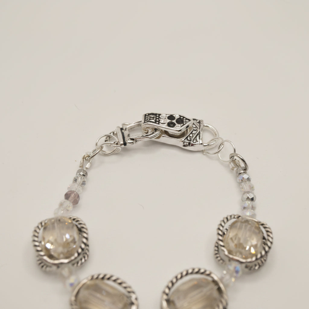 A silver-toned bracelet featuring three large oval clear crystals in textured bezel settings, separated by small clear faceted beads, photographed on a plain light gray background.
