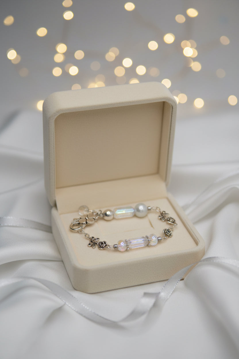 A silver-toned beaded bracelet featuring iridescent white beads, small pearl-like beads, and a silver-toned floral clasp, displayed on a plain gray background.