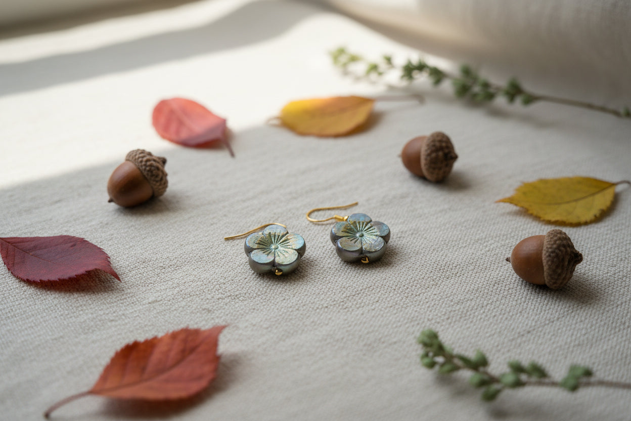 A pair of flower-shaped dangling earrings with gold hooks and iridescent petals in brown, yellow, and green tones, displayed against a light gray background.