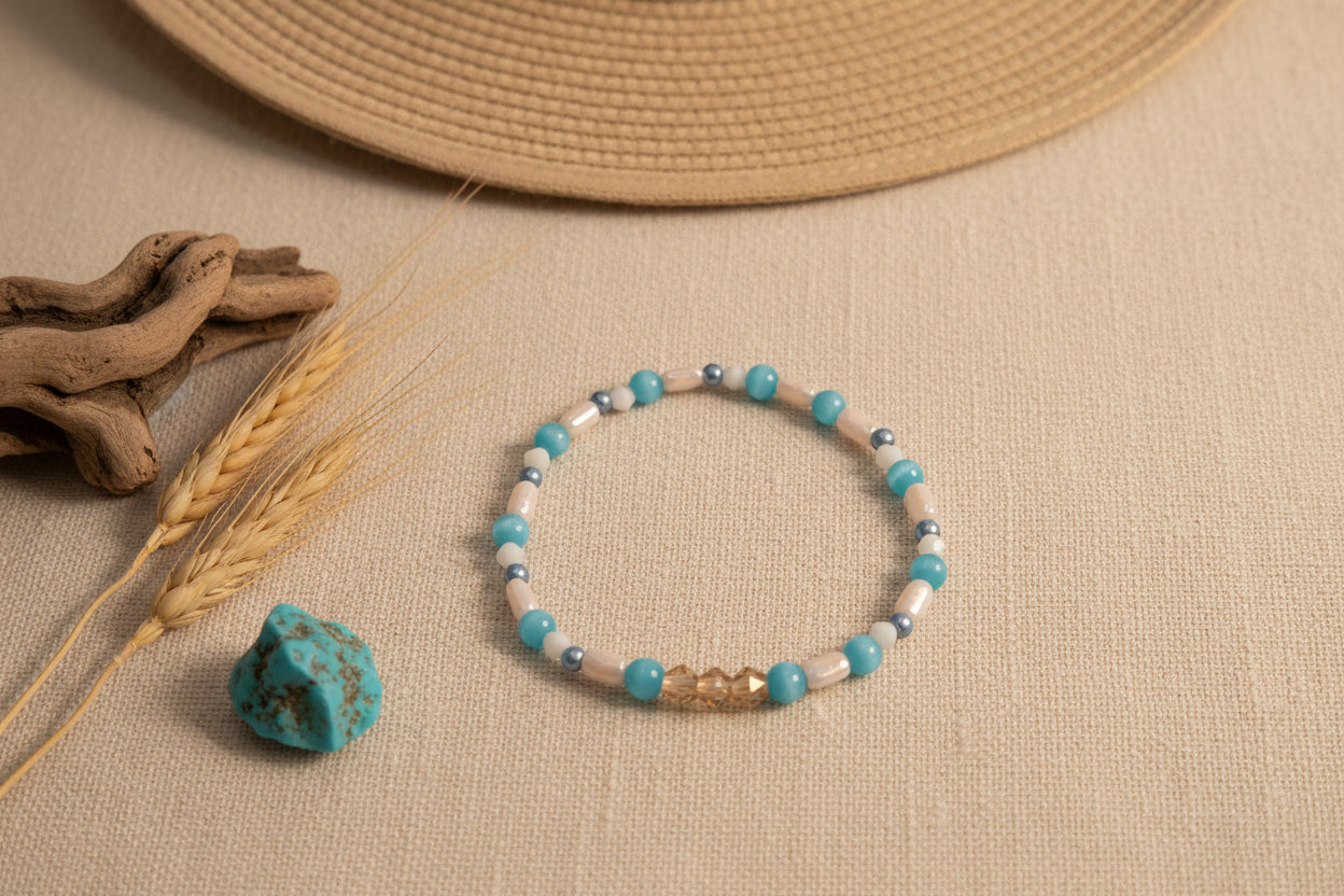 A beaded stretch bracelet featuring turquoise blue beads, cream-colored stone beads, small silver spacer beads, and a central gold-toned geometric charm, displayed on a neutral gray background.