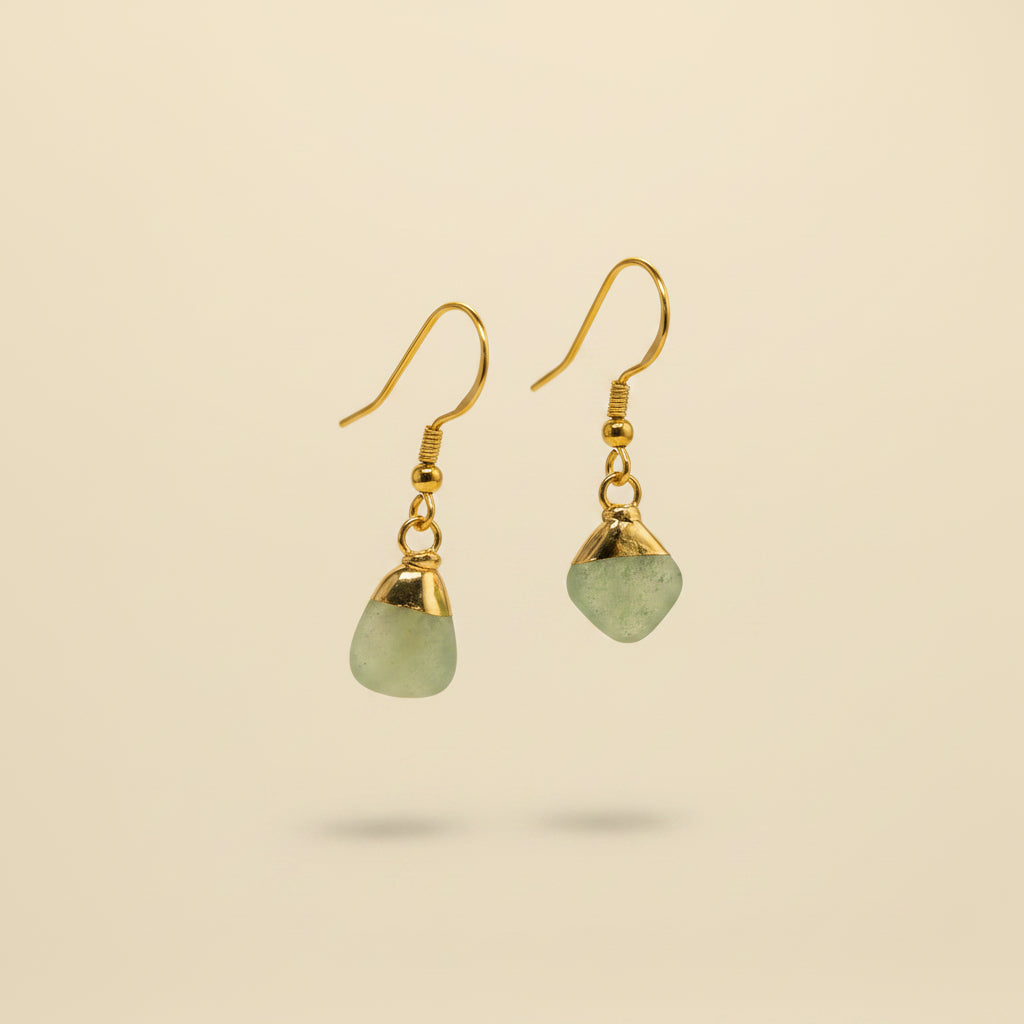 A pair of gold drop earrings with irregular light green stone pendants, displayed on a clear plastic stand against a neutral gray background.