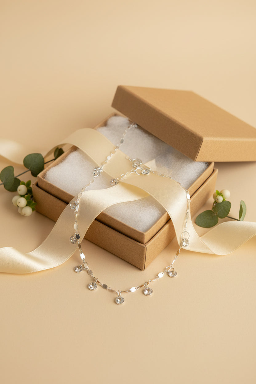 A silver-toned beaded necklace with small dangling charms, displayed on a black velvet jewelry bust against a white background.