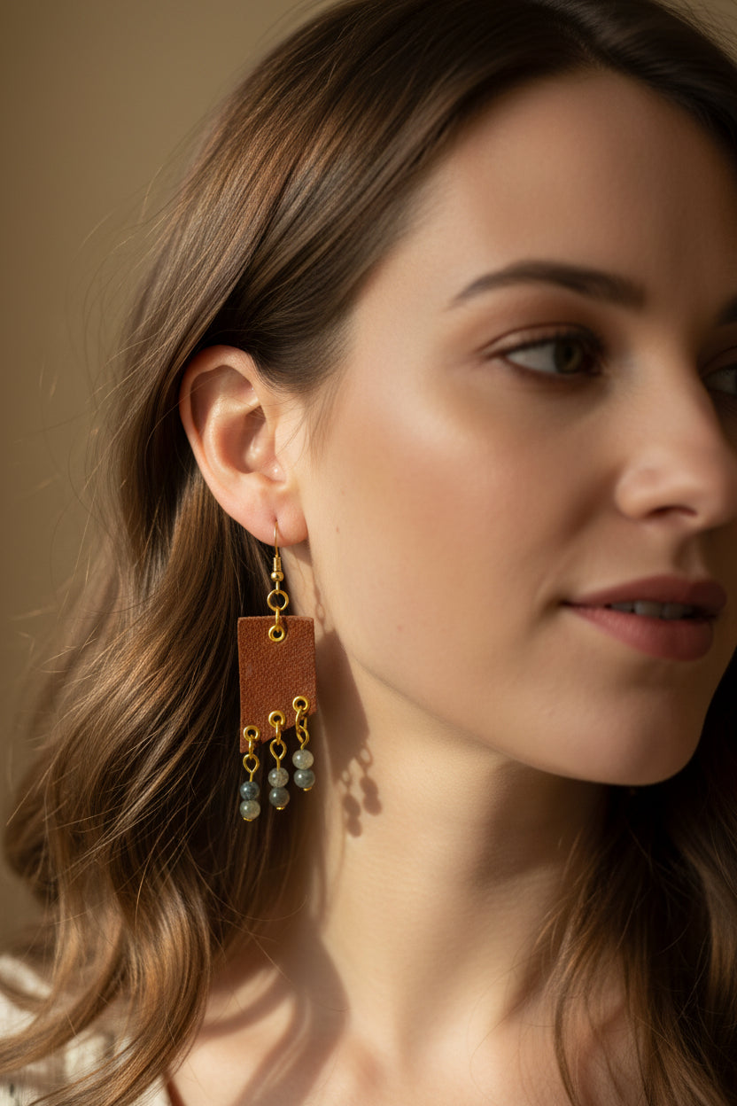 Brown leather earrings with gold accents and green beads on a white background