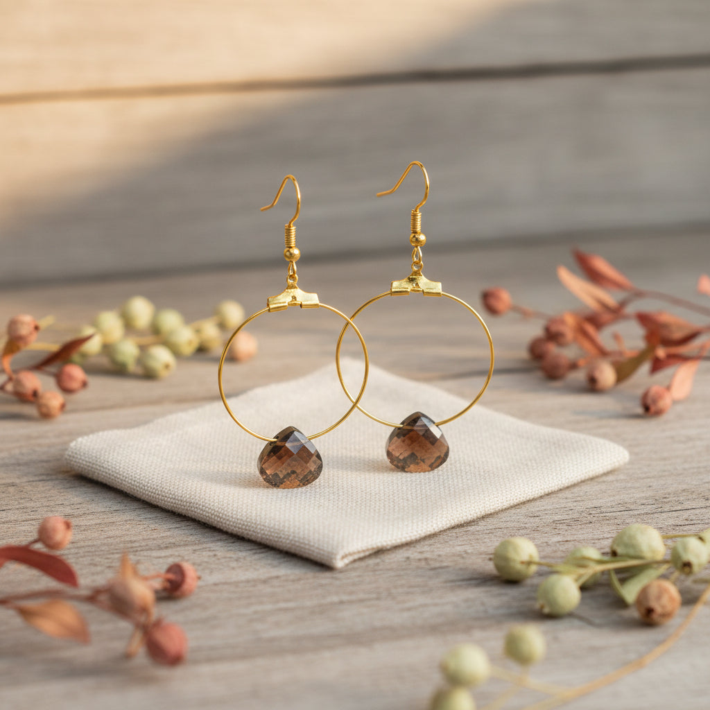 A pair of gold hoop earrings with faceted brown heart-shaped pendants, displayed on a clear plastic stand against a light gray background.