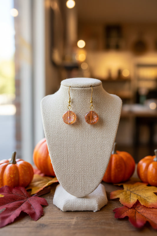 A pair of gold-tone leverback earrings with round, textured amber-orange glass pendants, displayed on a clear acrylic stand against a neutral gray background.