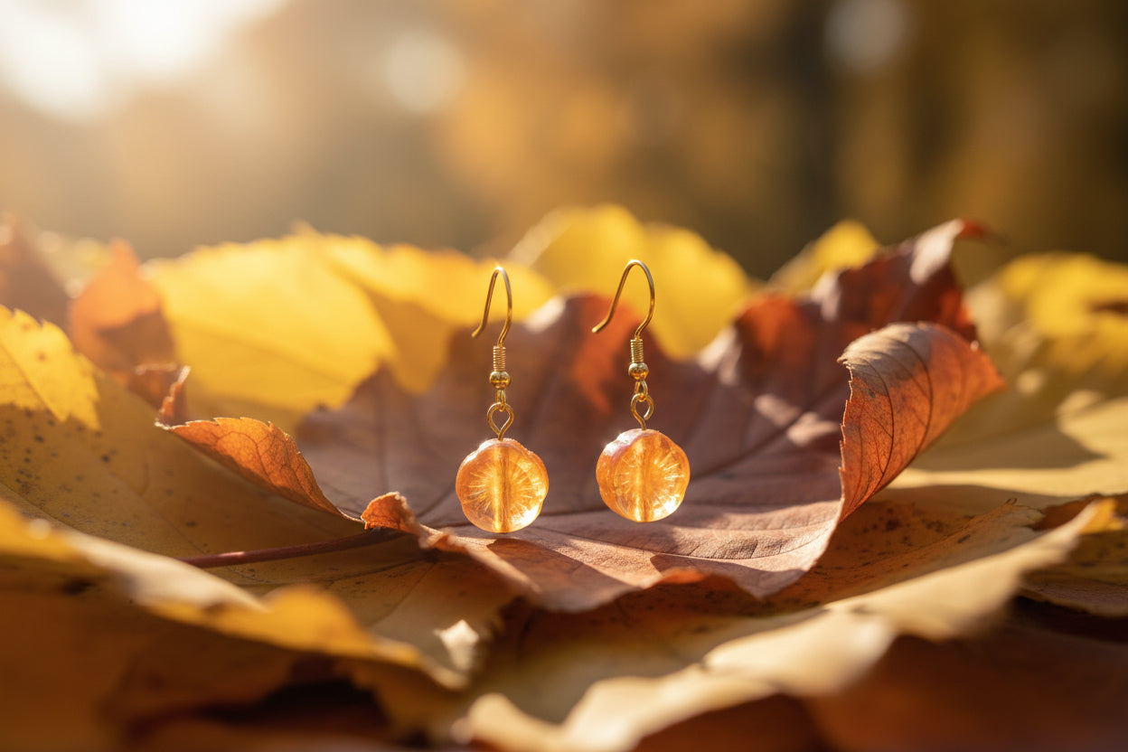 A pair of gold-tone dangle earrings with round, textured orange and pink glass pendants, displayed on a clear acrylic stand against a neutral gray background.