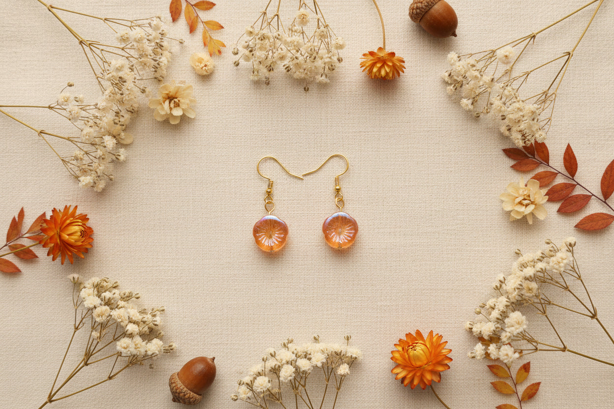 A pair of gold-tone dangle earrings with round, textured amber-orange beads, displayed on a clear acrylic stand against a solid gray background.