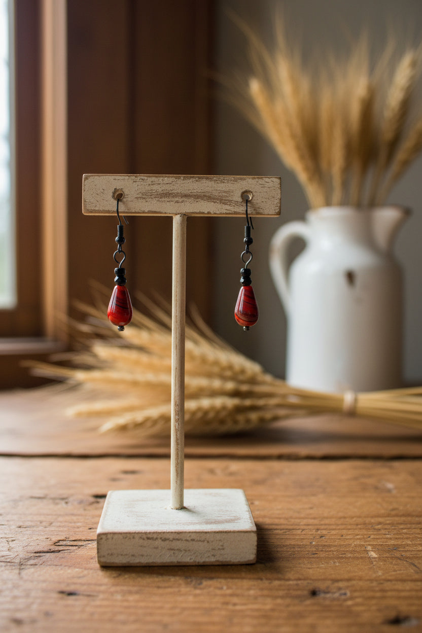 A pair of dangle earrings with teardrop-shaped red and black marbled beads, suspended from black metal hooks, displayed against a light gray background.