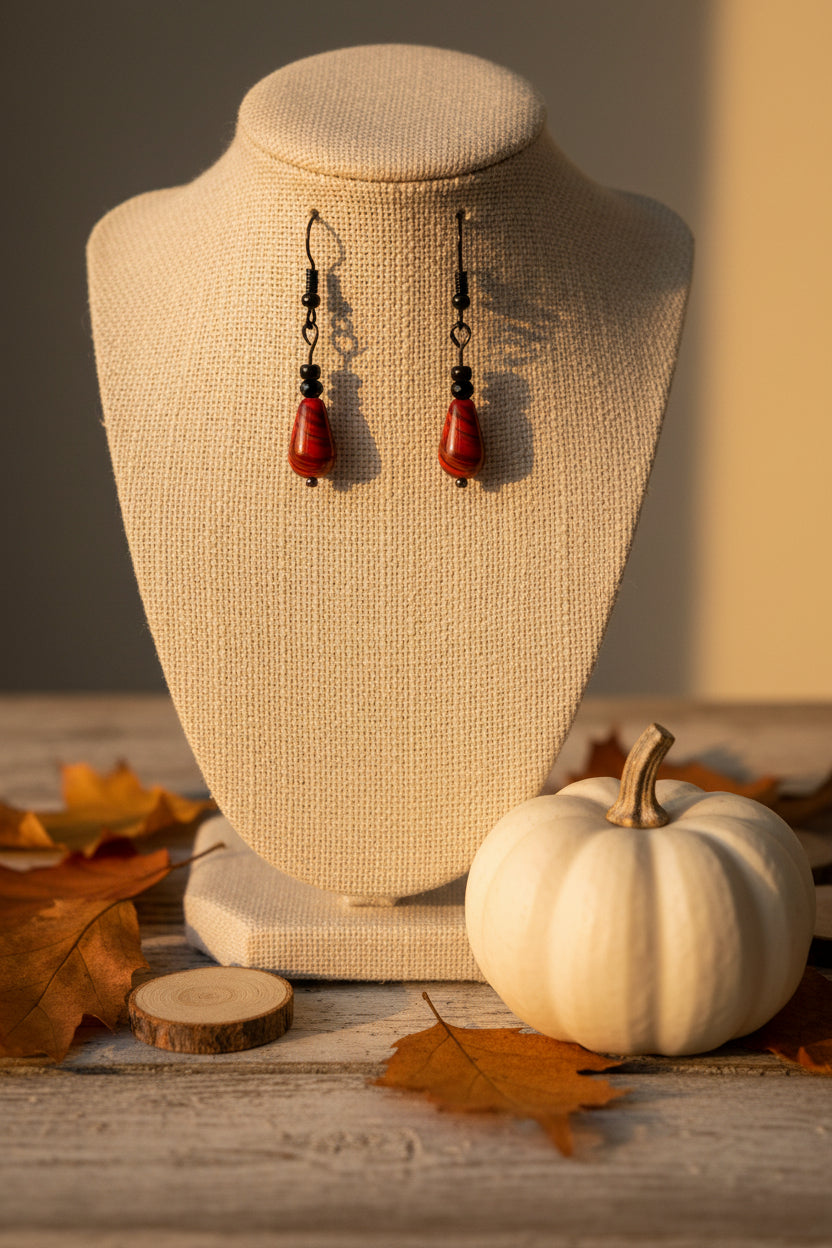 A pair of handmade dangle earrings with teardrop-shaped red and black marbled beads suspended from black wire hooks, displayed against a neutral gray background.