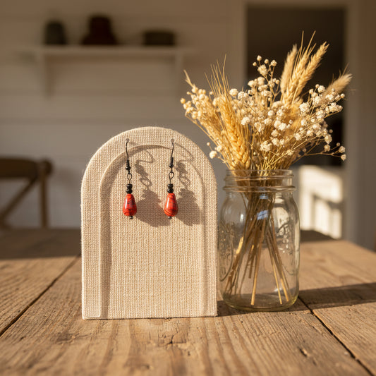 A pair of handmade dangle earrings with teardrop-shaped red and black marbled beads, suspended from black wire hooks with small black beads, shown against a neutral gray background.