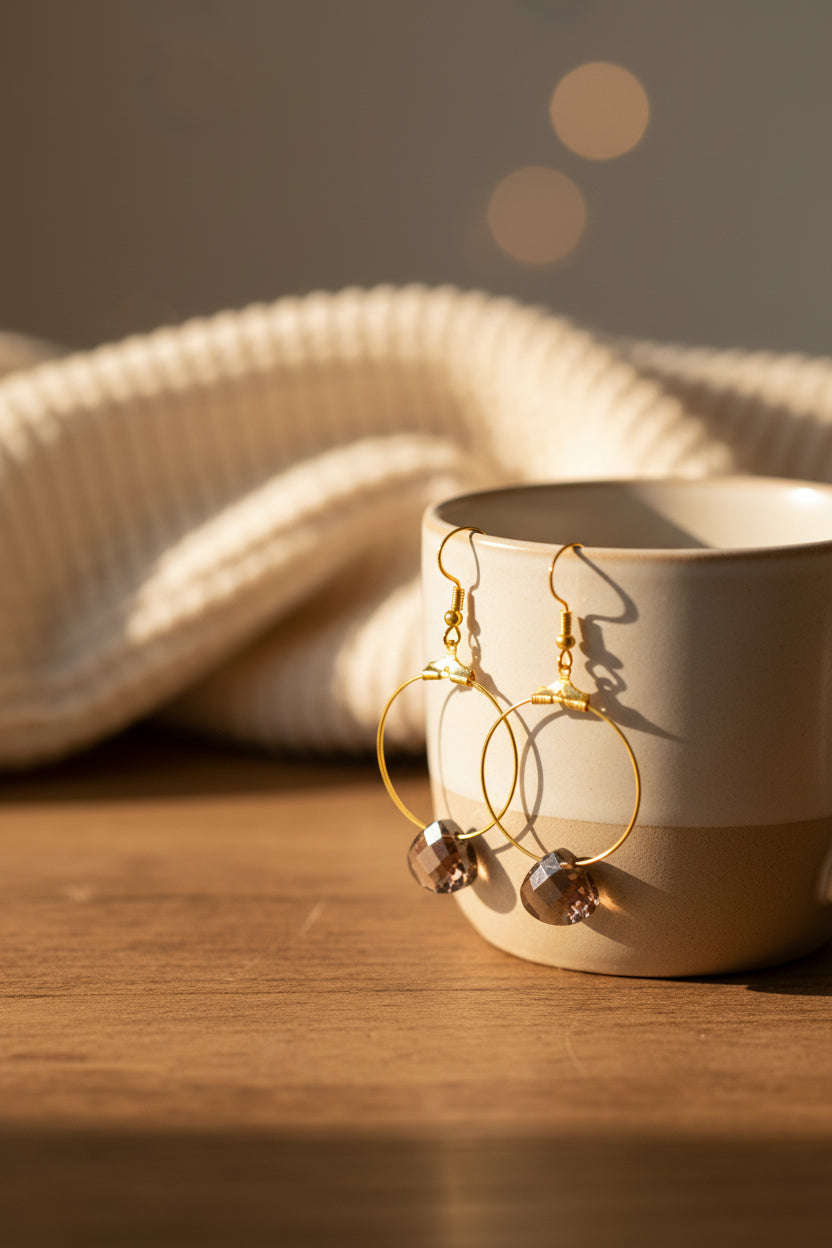 A pair of gold hoop earrings with faceted brown smoky quartz stones, hanging from gold French hooks against a light gray background.
