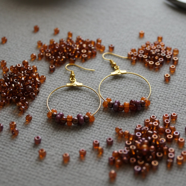 Gold hoop earrings with brown beads on a 'River Inspired' branded card.