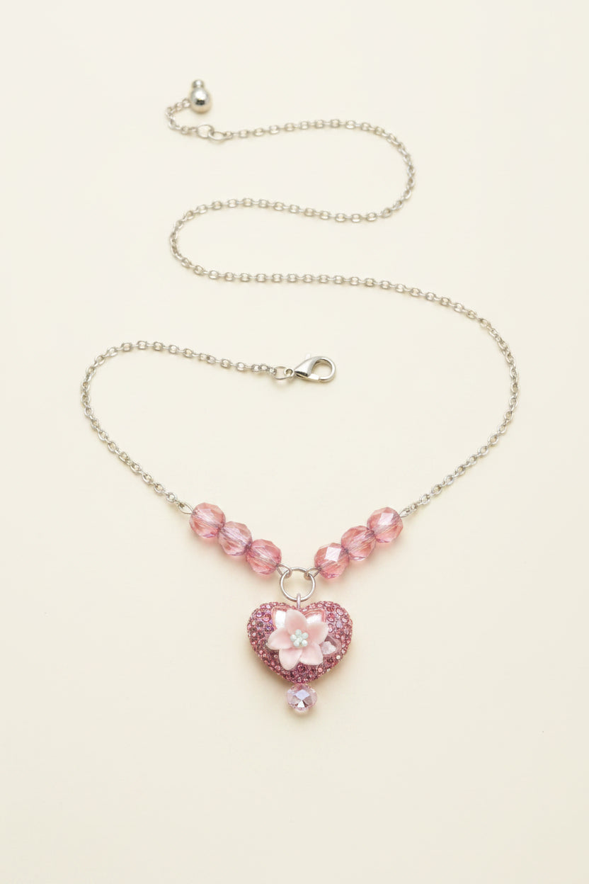 A silver chain necklace with pink faceted beads and a pink rhinestone-embellished heart pendant, displayed on a black velvet necklace bust.