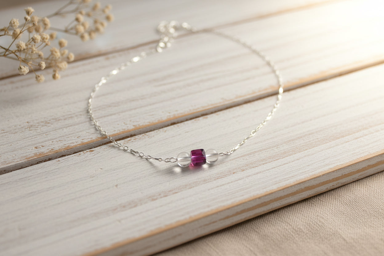 A silver chain necklace with three small beads, including two pinkish-red faceted beads and one clear faceted bead, displayed on a black velvet jewelry bust against a white background.