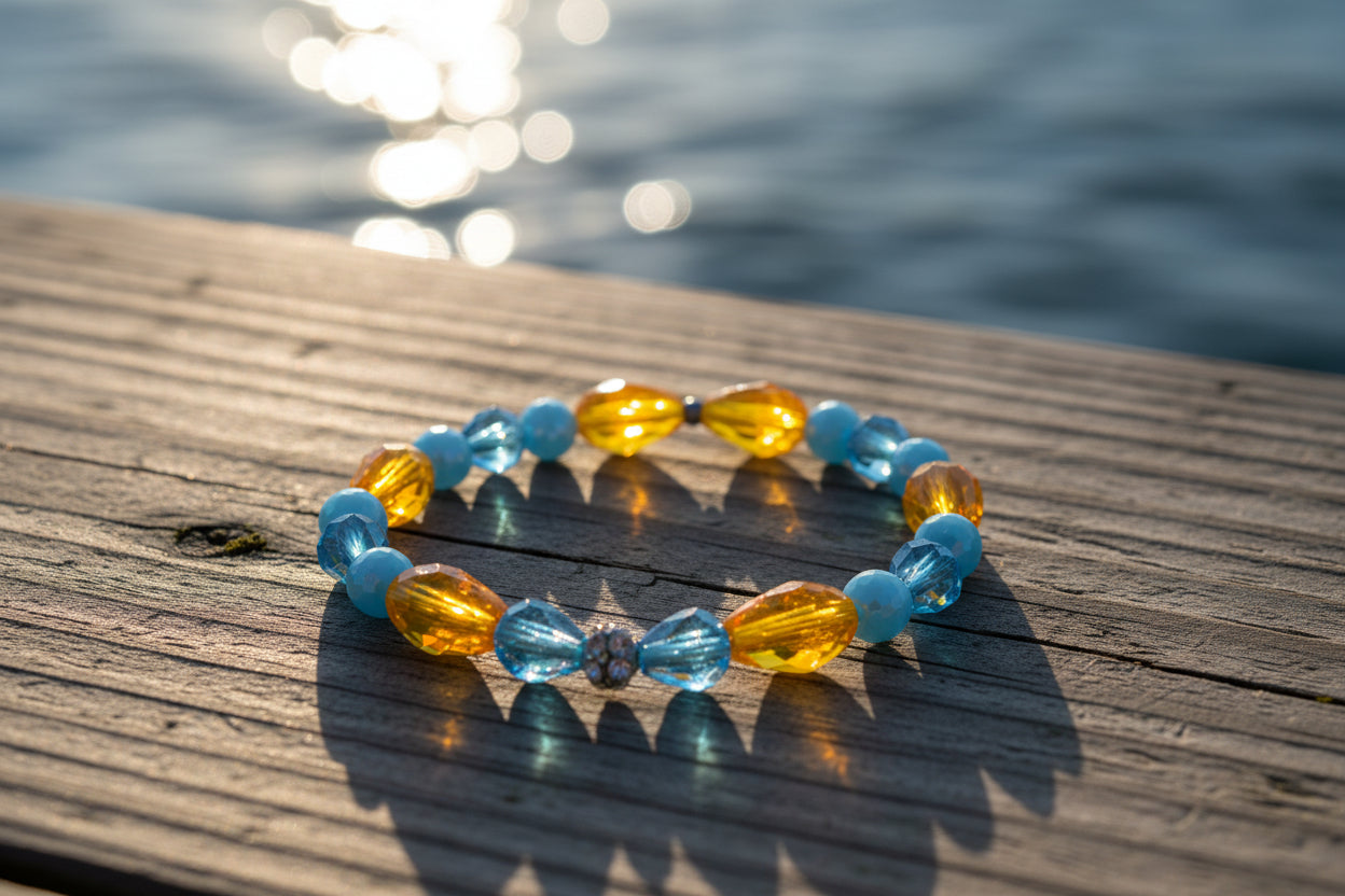 A beaded stretch bracelet featuring faceted light blue beads and larger translucent amber-yellow teardrop beads, with a small silver-toned decorative bead at the center, displayed on a neutral light gray background.