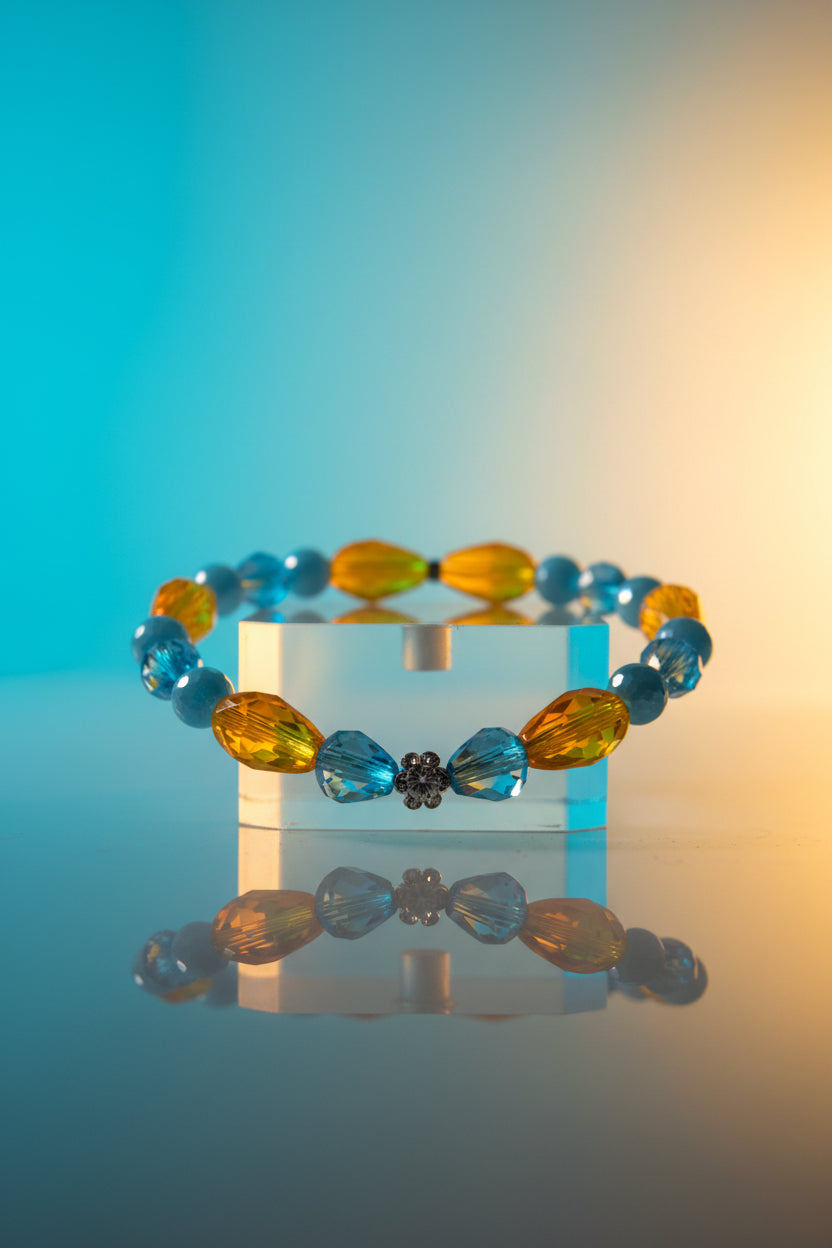 A beaded stretch bracelet featuring faceted light blue and translucent amber-yellow beads, with a small clear rhinestone accent at the bottom center, displayed on a neutral light gray background.