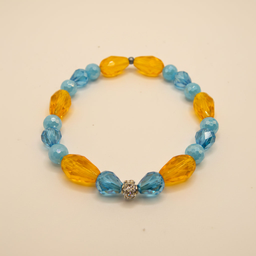 A beaded stretch bracelet featuring faceted light blue beads and larger translucent amber-yellow teardrop beads, with a small silver-toned bead accent at the front, displayed on a neutral light gray background.