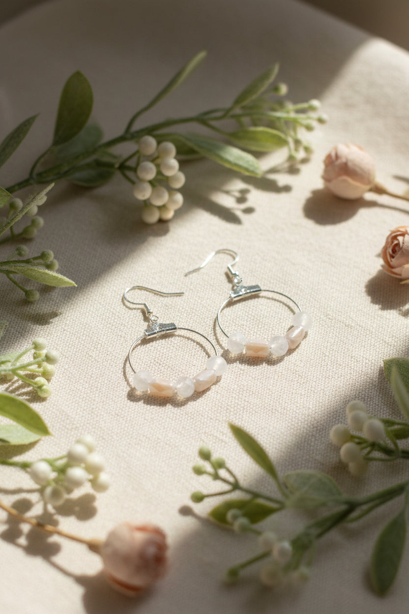 A pair of silver hoop earrings with small pale pink and white beads hanging from silver fishhook wires, displayed against a light gray background.