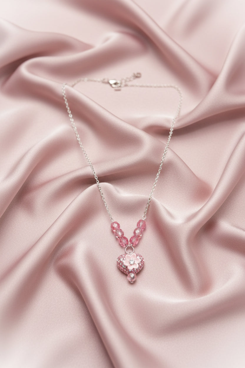 A pink beaded necklace with a heart-shaped rhinestone pendant, displayed on a black velvet jewelry bust against a white background.