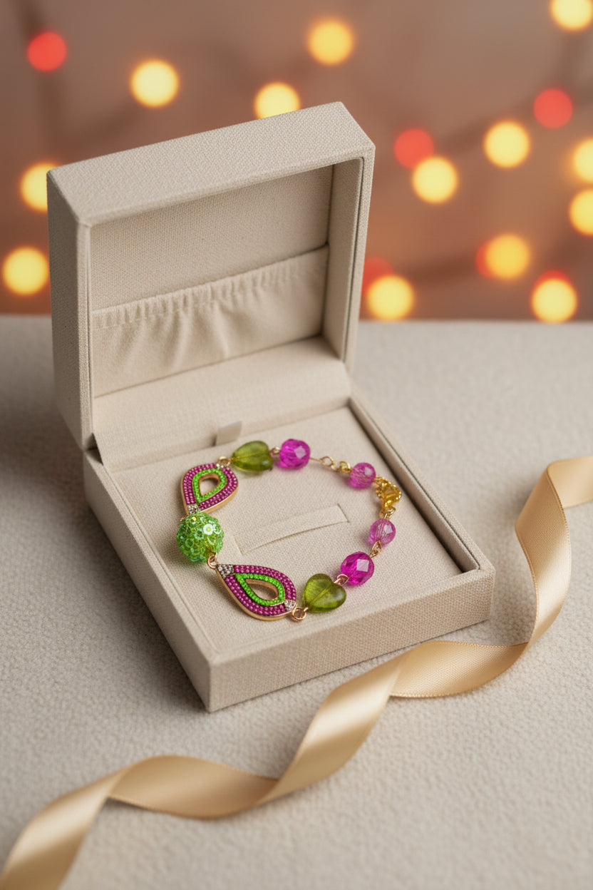 A handmade beaded bracelet featuring green heart-shaped beads, pink flower beads, a green faceted bead, and pink mesh teardrop charms with gold-tone metal findings, displayed on a plain light gray surface.