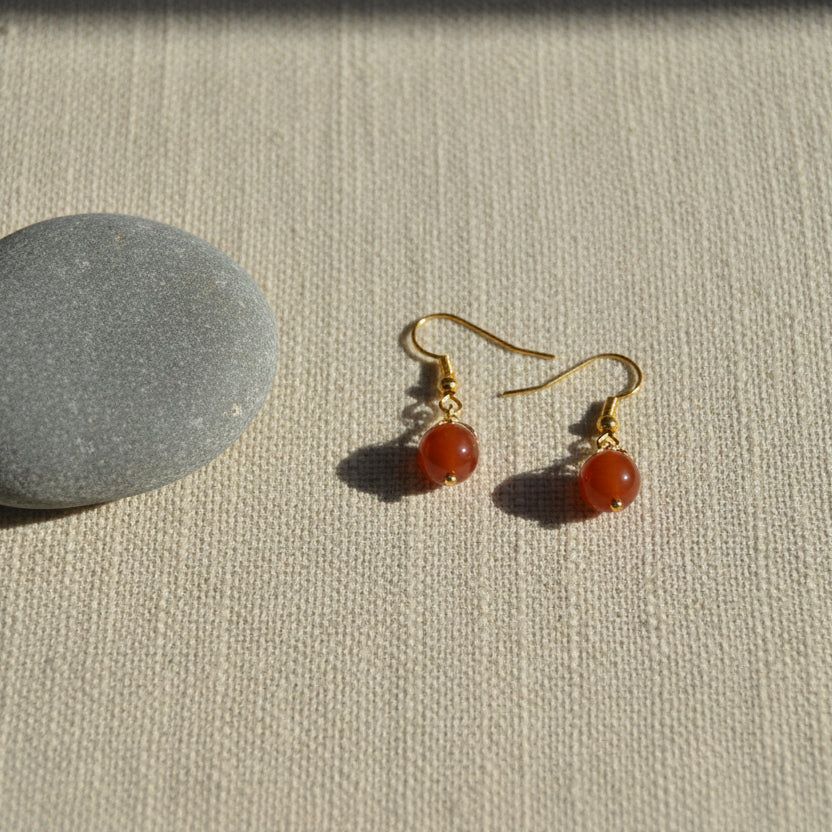 Gold earring with a red gemstone on a gray background