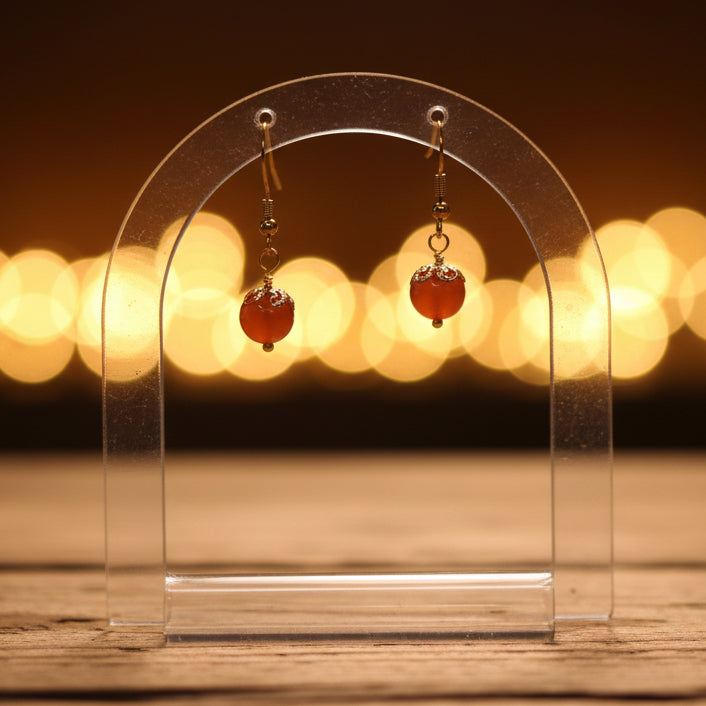 Gold earrings with red beads on a gray background
