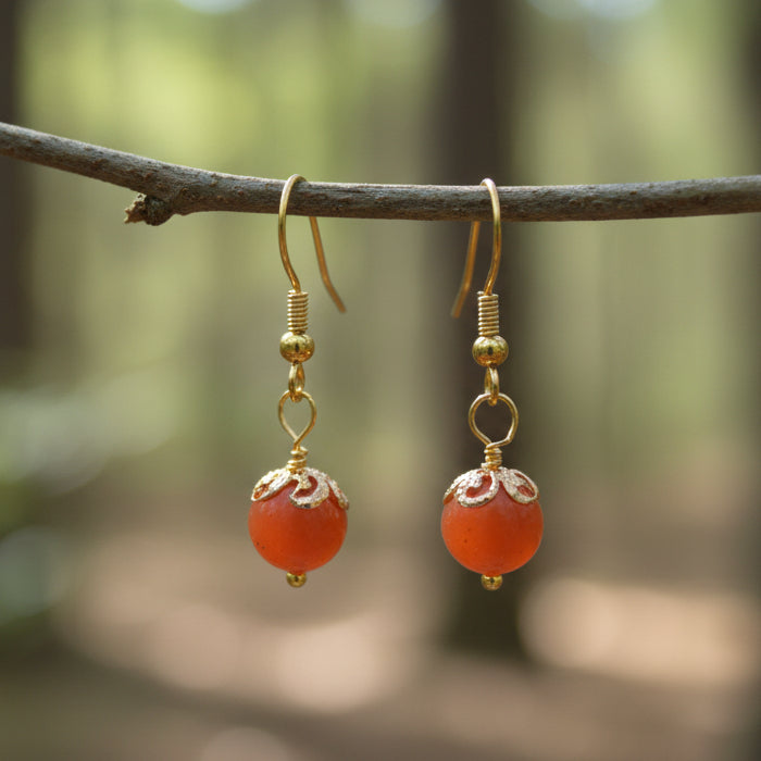 Pair of gold earrings with red beads on a gray background
