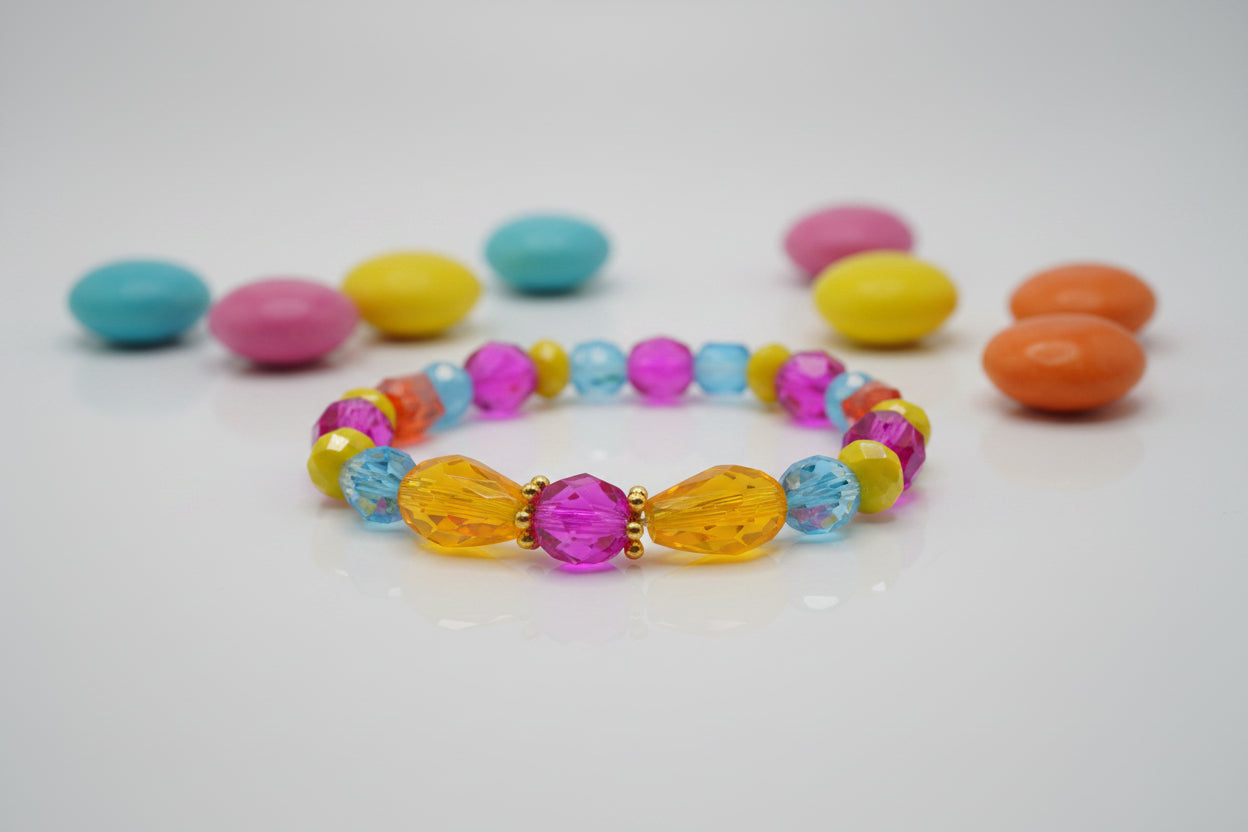 A colorful beaded stretch bracelet featuring faceted round beads in pink, blue, yellow, and orange, with two larger teardrop-shaped yellow beads and a central pink faceted bead, displayed on a neutral gray background.