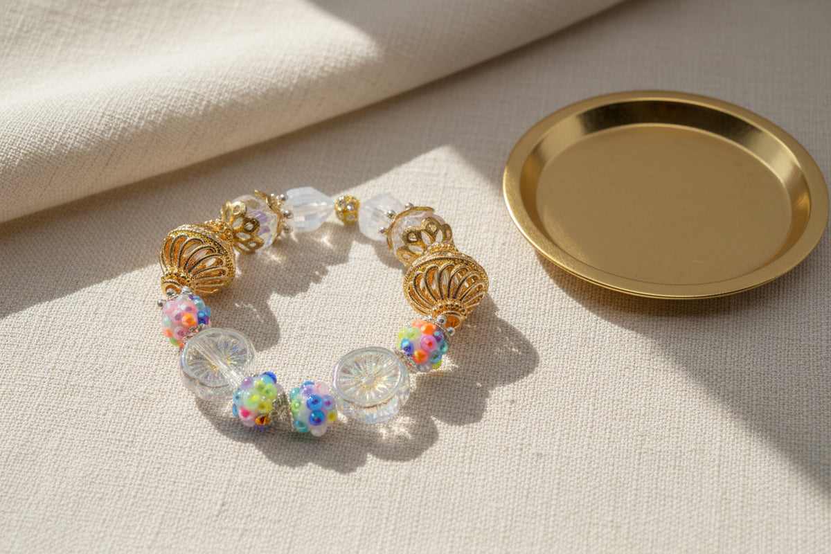 A beaded bracelet featuring gold filigree beads, clear glass beads, and several iridescent multicolor beads, displayed on a neutral gray background.