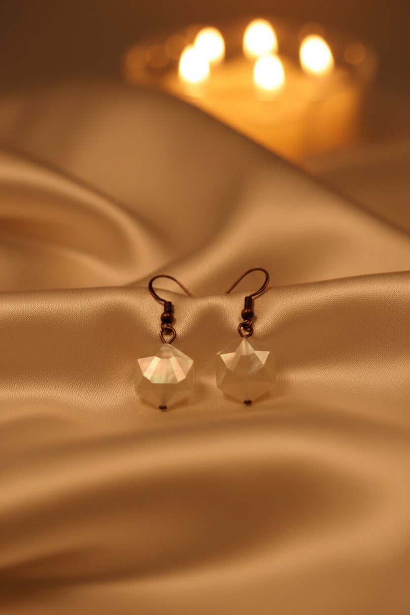 A pair of geometric drop earrings with faceted cream-colored beads and dark metal hooks, displayed against a neutral gray background.