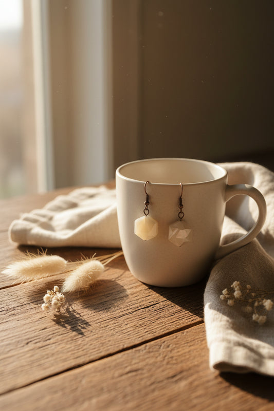 A pair of handmade dangle earrings featuring faceted, translucent cream-colored beads suspended from dark metal wire hooks, displayed against a neutral light gray background.