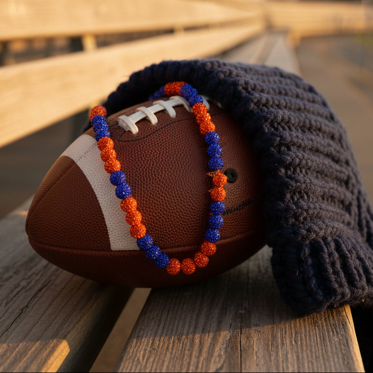 A beaded necklace or bracelet made of alternating translucent blue and orange-red faceted beads, arranged in a circle on a plain light gray background.