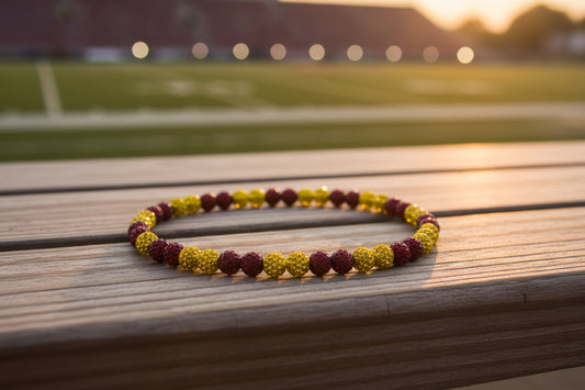 A beaded necklace made of alternating dark red faceted beads and metallic gold textured beads, arranged in a circle on a plain white surface.