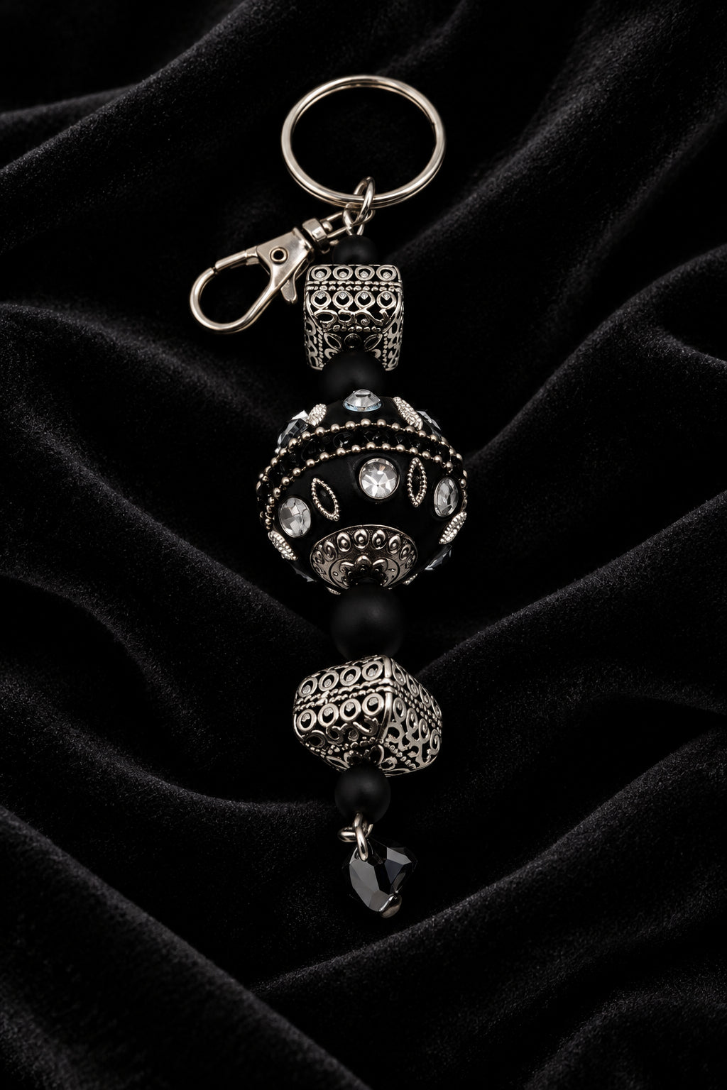 A beaded keychain featuring black beads, textured silver-toned spacer beads, and a silver lobster clasp, shown on a plain light gray background.