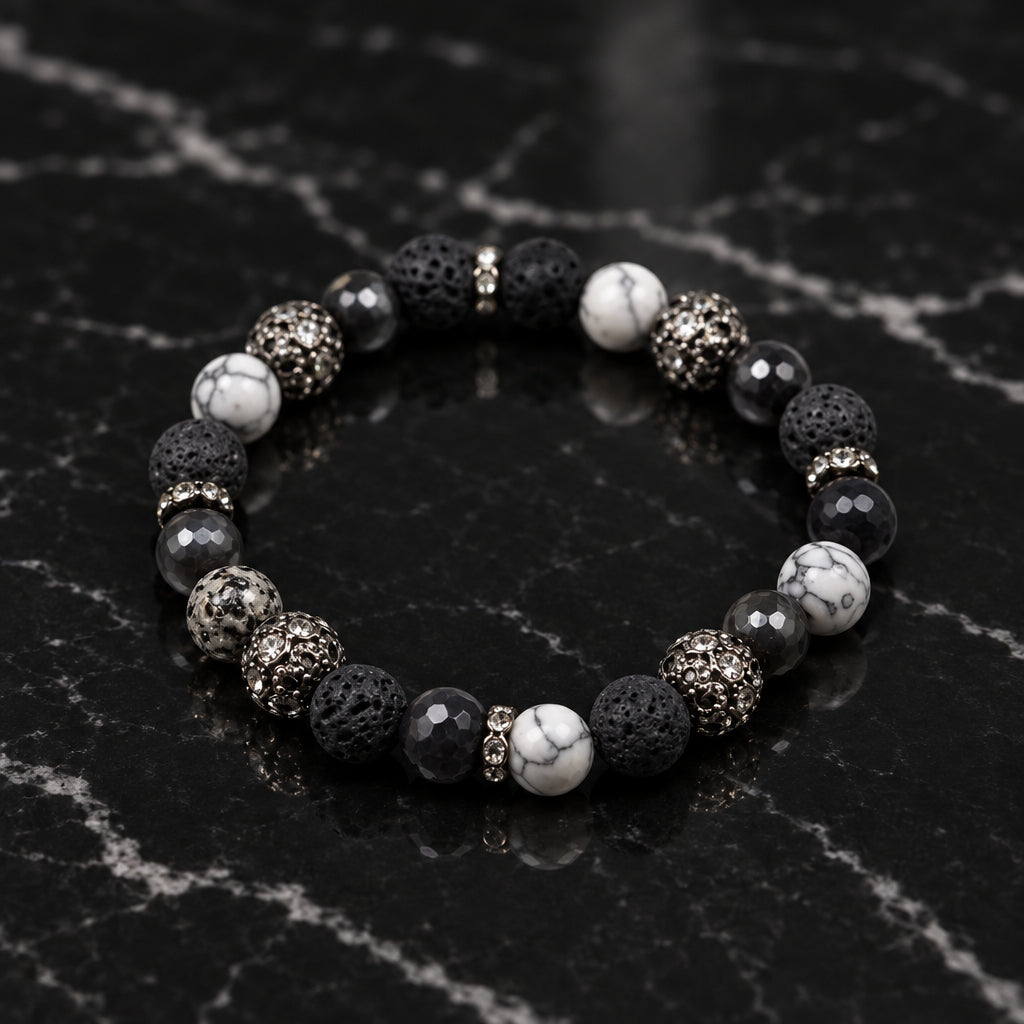 A beaded stretch bracelet featuring black, gray, and white marbled round beads, with textured metallic spacer beads, displayed on a neutral light gray background.