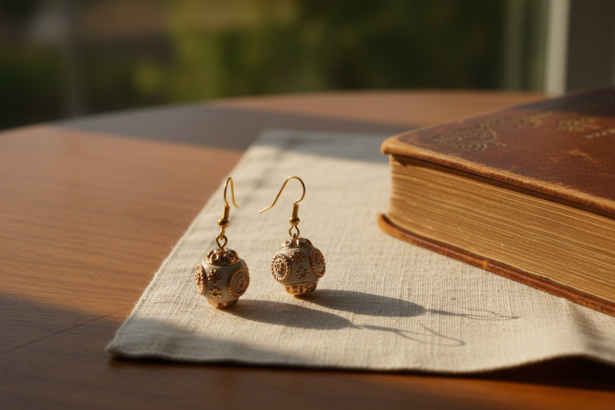 A pair of dangling earrings with gold-tone hooks and spherical, openwork filigree charms in a warm peach-pink tone, displayed against a light gray background on a clear stand.