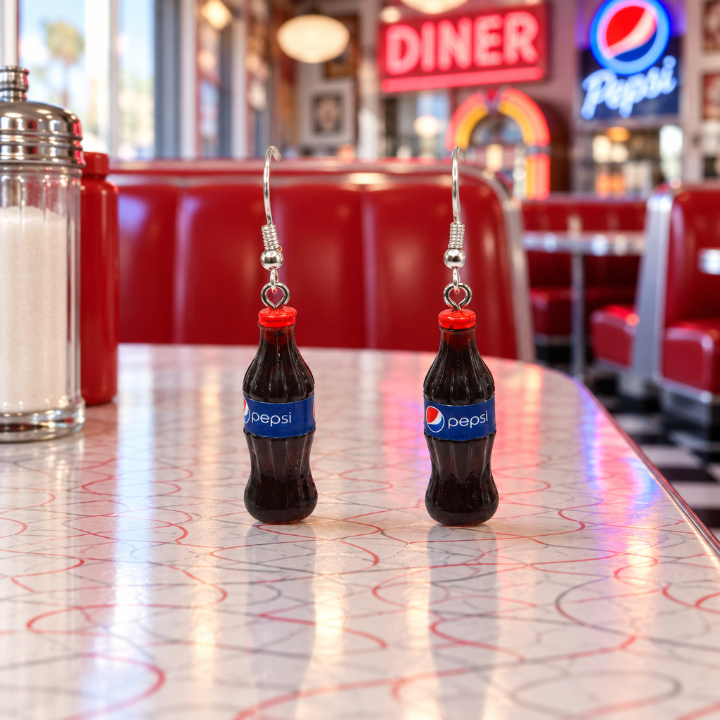 A pair of novelty earrings shaped like miniature Pepsi-Cola bottles, hanging from silver fishhook wires against a plain light gray background.