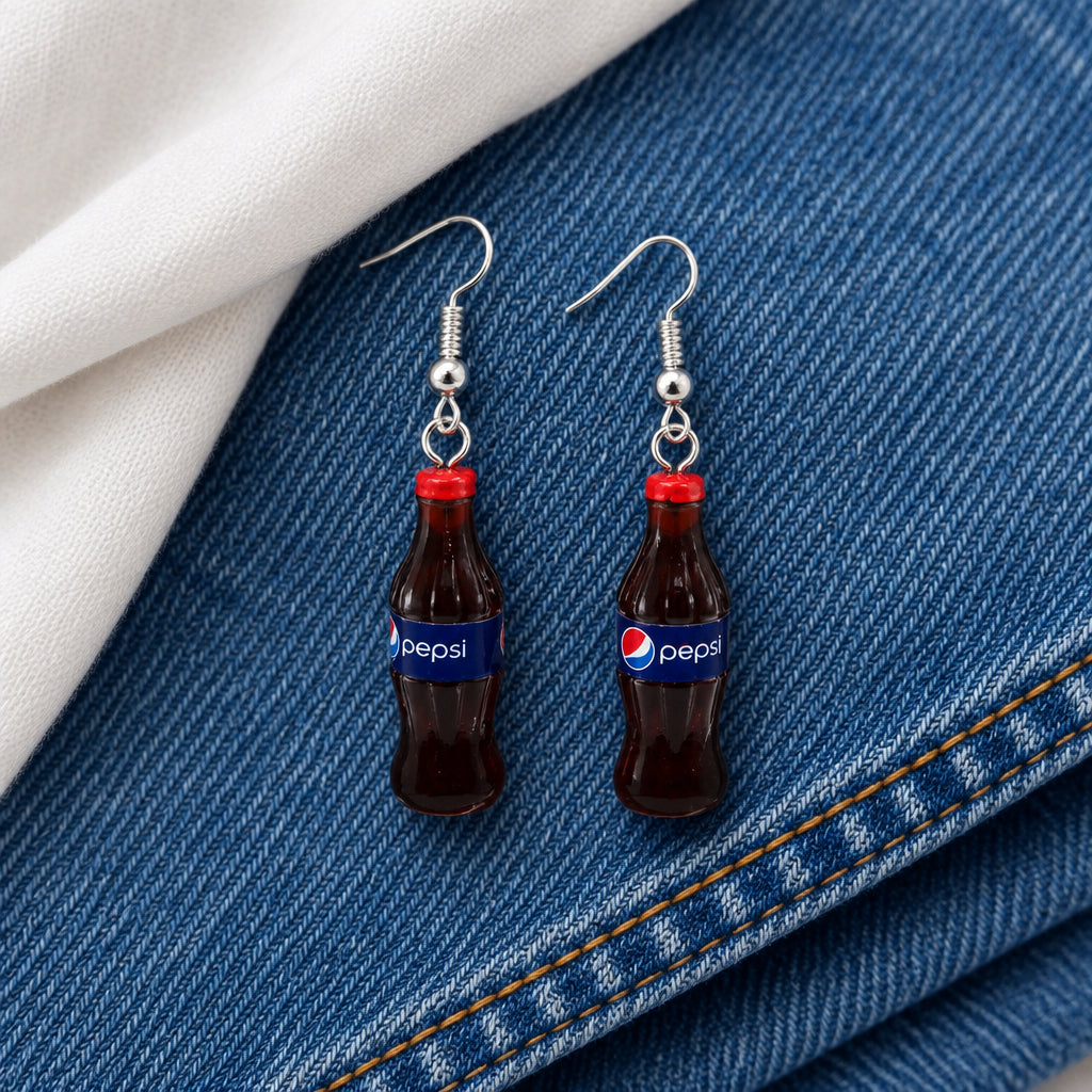 A pair of novelty earrings shaped like miniature Pepsi-Cola bottles with silver fishhook wires, displayed on a clear stand against a neutral gray background.