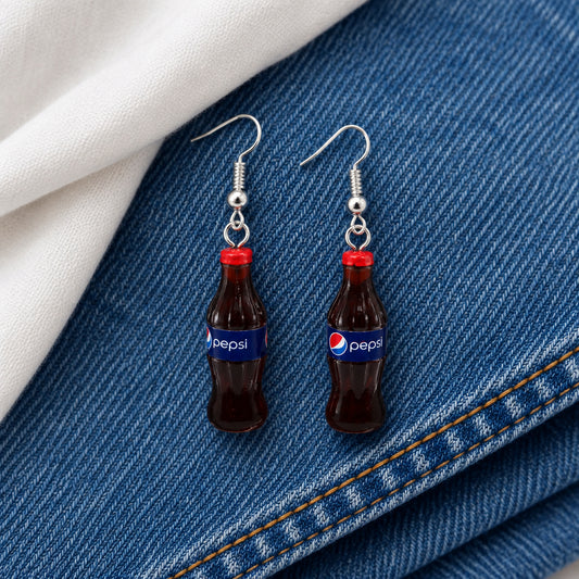 A pair of novelty earrings shaped like miniature Pepsi-Cola bottles with silver fishhook wires, displayed on a clear stand against a neutral gray background.