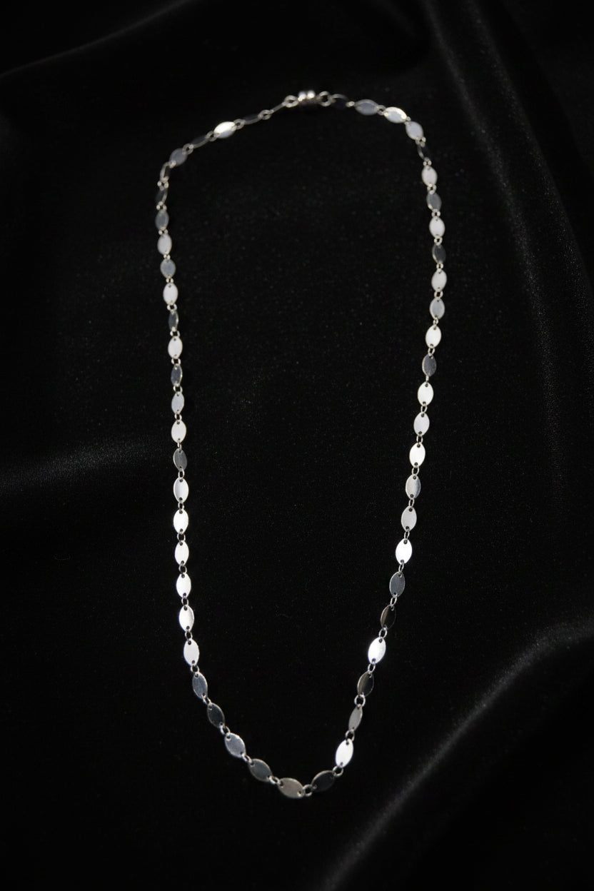 A delicate silver chain necklace with elongated oval links, displayed against a plain light gray background.