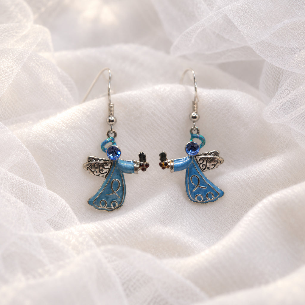 A pair of dangling angel earrings displayed on a clear plastic stand against a light gray background. The earrings feature light blue enamel angel figures with silver-toned metal wings and hooks, accented by small dark blue and green beads.