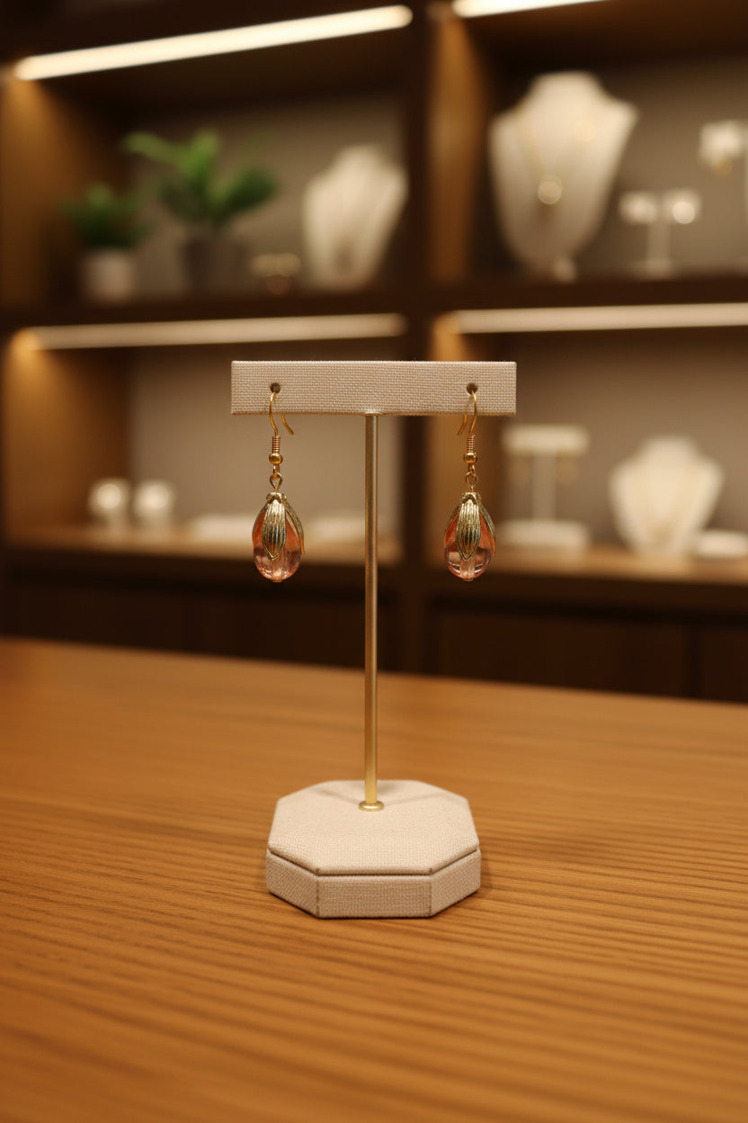 A pair of gold-tone dangle earrings with translucent pink and white bead drops, displayed on a clear acrylic stand against a light gray background.